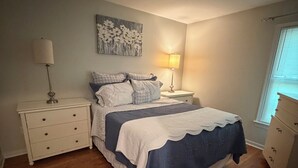 Un dormitorio con cama, dos mesitas de noche, un tocador y un armario, además de una ventana con persianas.