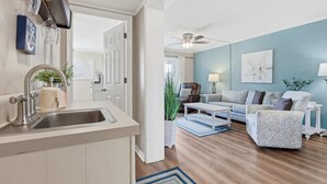 A modern kitchen with a sink, a ceiling fan, and a dining area with a table and chairs. - Sea Cabin Shores w Pool View and Ocean Peek (North Myrtle Beach)