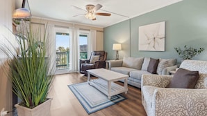 A living room with a sofa, armchair, coffee table, and a potted plant. - Sea Cabin Shores w Pool View and Ocean Peek (North Myrtle Beach)