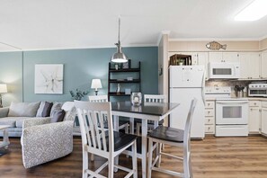 Une cuisine moderne avec des meubles blancs, un réfrigérateur blanc, un four à micro-ondes et une cuisinière. On y trouve une table à manger avec des chaises et un luminaire suspendu au-dessus.