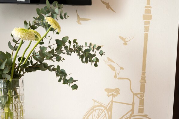 A wall with a bicycle and birds, a vase with flowers, and a television.