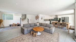 Ein modernes Wohnzimmer mit einem Ecksofa, einem runden Couchtisch und einem Essbereich mit Holztisch und Stühlen.