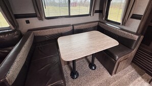 A compact RV interior with a dining table, cushioned seating, and large windows. - Haven on Wheels- Cozy Travel Trailer Getaway in Nature (Williamston)