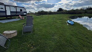 A grassy area with a camper, a hammock, and a kayak by a calm body of water. - Haven on Wheels- Cozy Travel Trailer Getaway in Nature (Williamston)