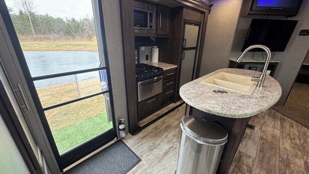 A modern kitchen with a large window, a sink, and a trash can. - Haven on Wheels- Cozy Travel Trailer Getaway in Nature (Williamston)