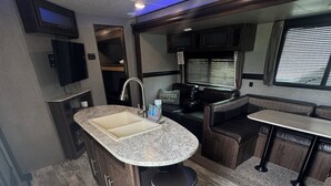 A compact RV kitchen with a sink, stove, and seating area. - Haven on Wheels- Cozy Travel Trailer Getaway in Nature (Williamston)