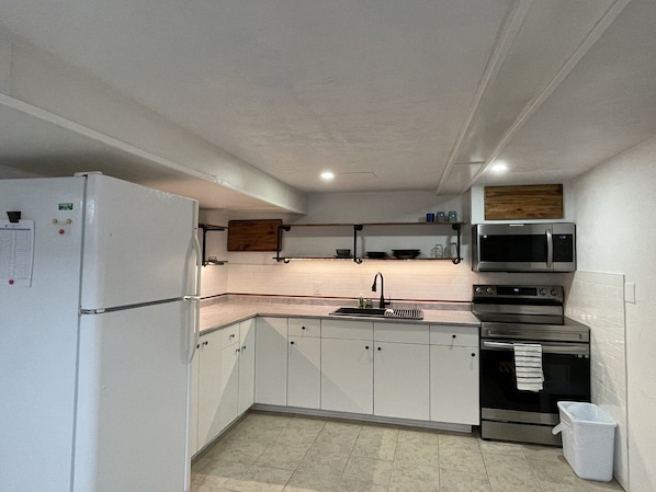 Una cocina con armarios blancos, un refrigerador de acero inoxidable, un microondas y un horno.