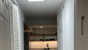 A narrow hallway leading to a kitchen with white cabinets, a chair, and a tiled floor. - Cozy Albert St Retreat (Waterloo)