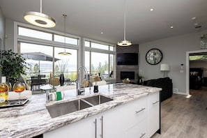 A modern kitchen with a large island, pendant lights, and a view to the outdoors. - "The Vino Vista" | 10 Acre Winery | Lakeview (Naramata)