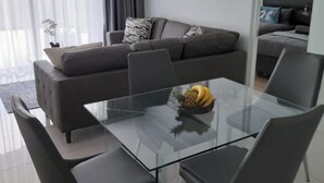 A modern living room with a glass dining table, grey sofa, and a painting on the wall.