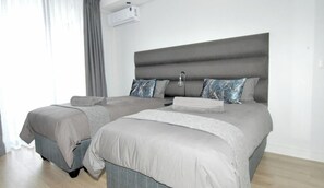 Ein Doppelbett mit grauer Bettwäsche, ein Nachttisch und eine Lampe.
