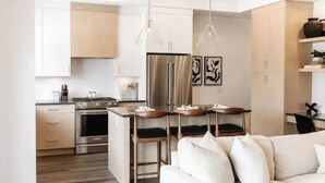 A modern kitchen with stainless steel appliances, a dining area with a table and chairs, and a living room with a sofa and pillows. - Luxury 4-bed, 3.5-bath home in Shelter Bay, West K,  rooftop deck with hot tub. (West Kelowna)
