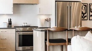 A modern kitchen with stainless steel appliances, wooden cabinets, and a dining area with white furniture. - Luxury 4-bed, 3.5-bath home in Shelter Bay, West K,  rooftop deck with hot tub. (West Kelowna)