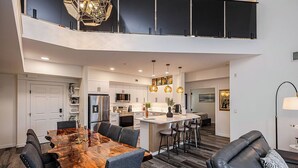 A spacious kitchen with a central island, a dining area with a large wooden table, and a living area with a sofa and a lamp.
