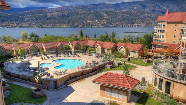 A hotel with a swimming pool, outdoor seating, and a view of a lake and mountains.