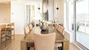 A modern dining area with a large wooden table, beige chairs, and a vase with flowers. - Skyfall 3 Bed 1 Den Lakeview Amenity Rich 30 Floor (Kelowna)