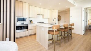 A modern kitchen with wooden cabinets, a built-in oven, and a central island with bar stools. - Skyfall 3 Bed 1 Den Lakeview Amenity Rich 30 Floor (Kelowna)