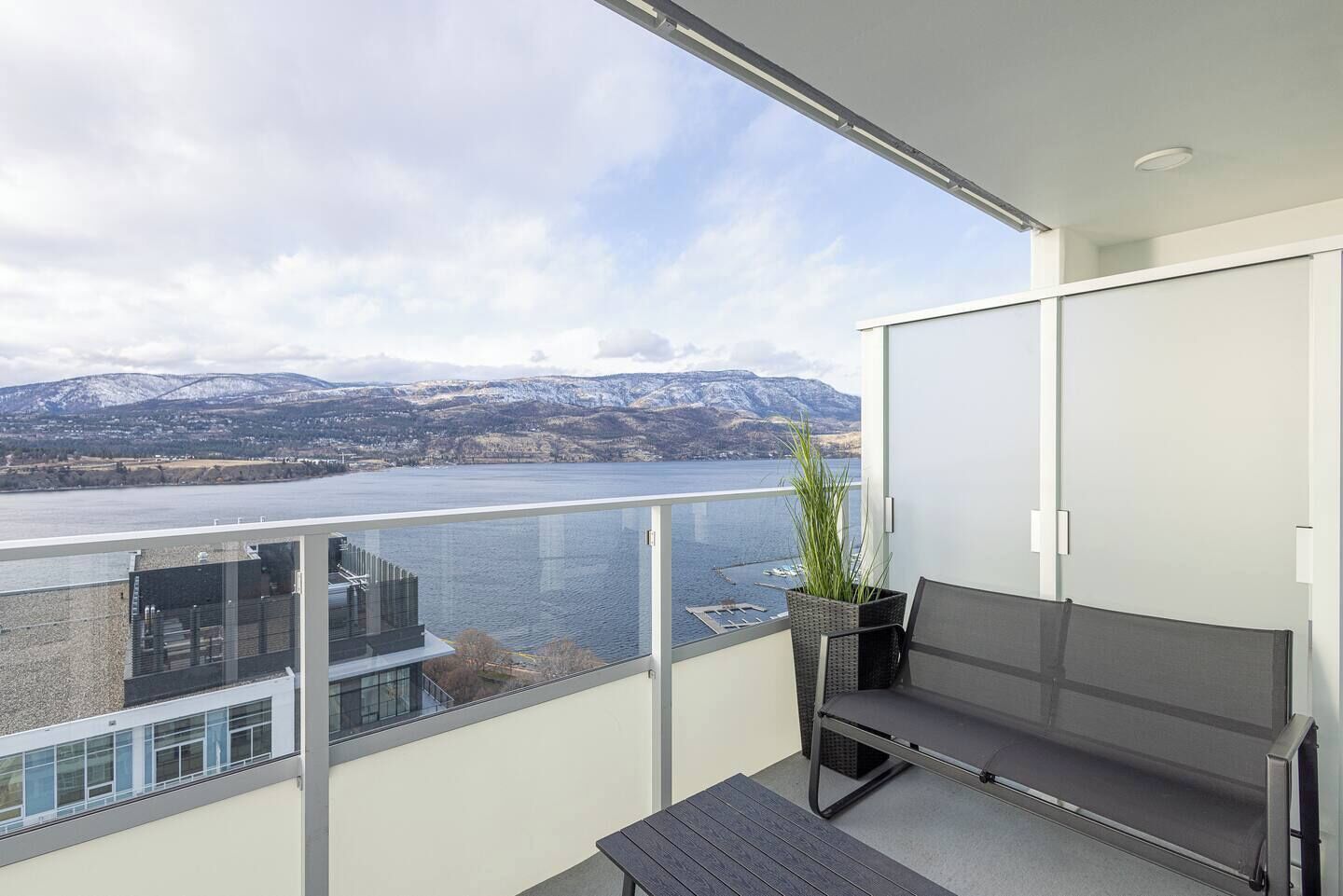 Un balcon avec vue sur un lac et des montagnes, un banc et une plante en pot.