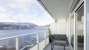 A balcony with a view of a lake and mountains, a bench, a potted plant, and a glass door. - Skyfall 3 Bed 1 Den Lakeview Amenity Rich 30 Floor (Kelowna)