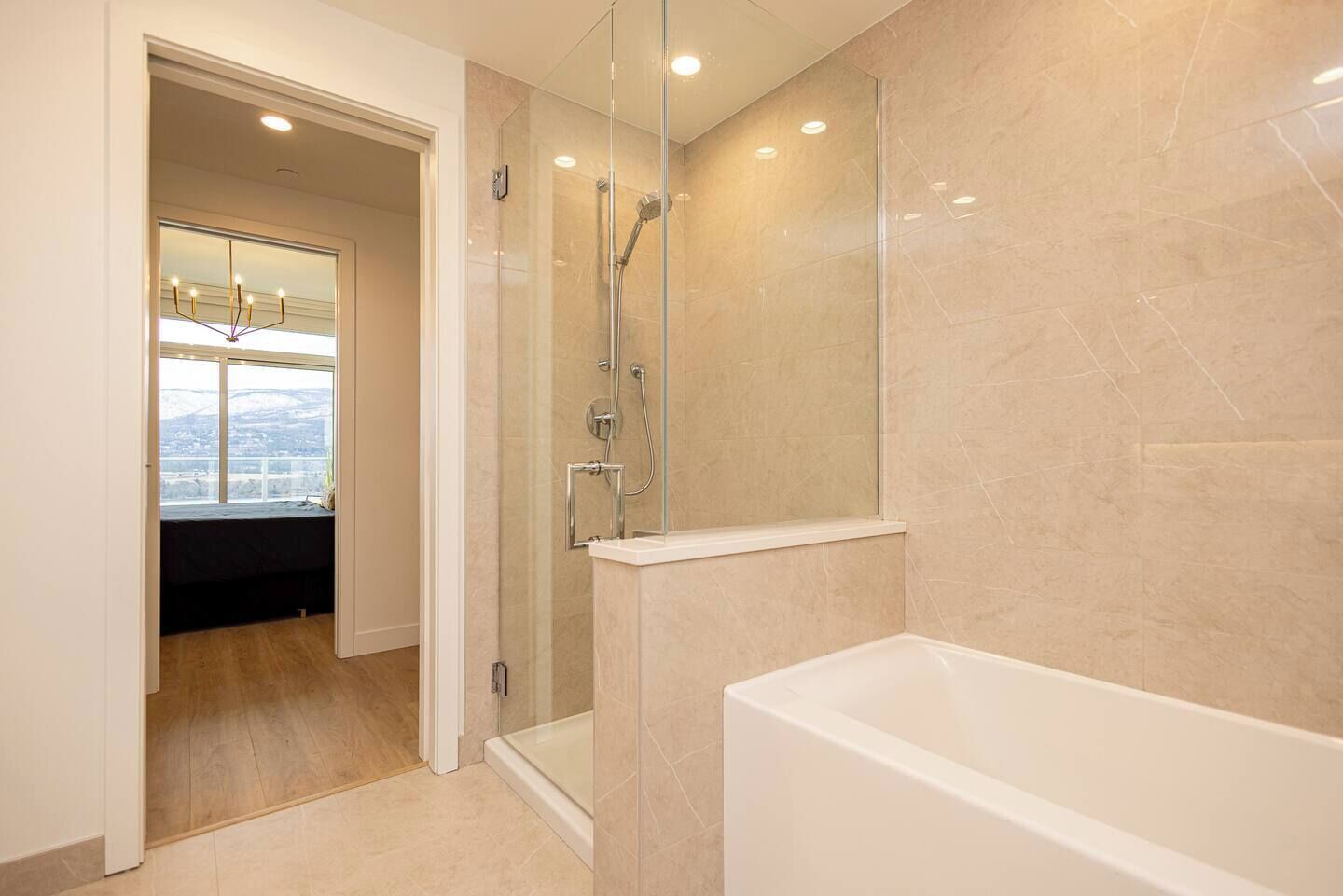 A modern bathroom with a glass-enclosed shower, a bathtub, and a view of a cityscape through a large window.