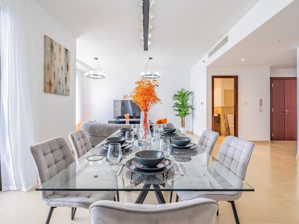 A modern dining area with a glass table, grey upholstered chairs, and a decorative vase.