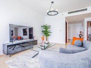 Ein modernes Wohnzimmer mit einem Glastisch, einem grauen Sofa, einem Flachbildfernseher und einer Topfpflanze.
