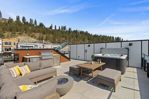 Um terraço no telhado com um sofá, uma mesa, churrasqueira e uma banheira de hidromassagem.
