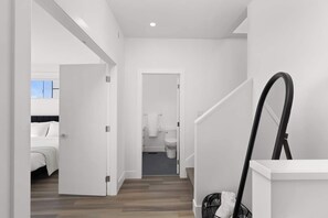 Quarto de hotel moderno com uma cama, banheiro com vaso sanitário e pia, e corredor com escada.