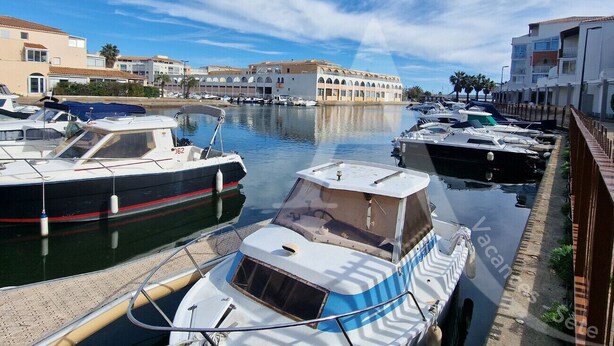 Un port de plaisance avec des bateaux amarrés, un ciel dégagé et des bâtiments en arrière-plan.