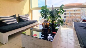 Un balcon avec un canapé en osier, une table basse en verre, une plante en pot et une vue sur les immeubles.