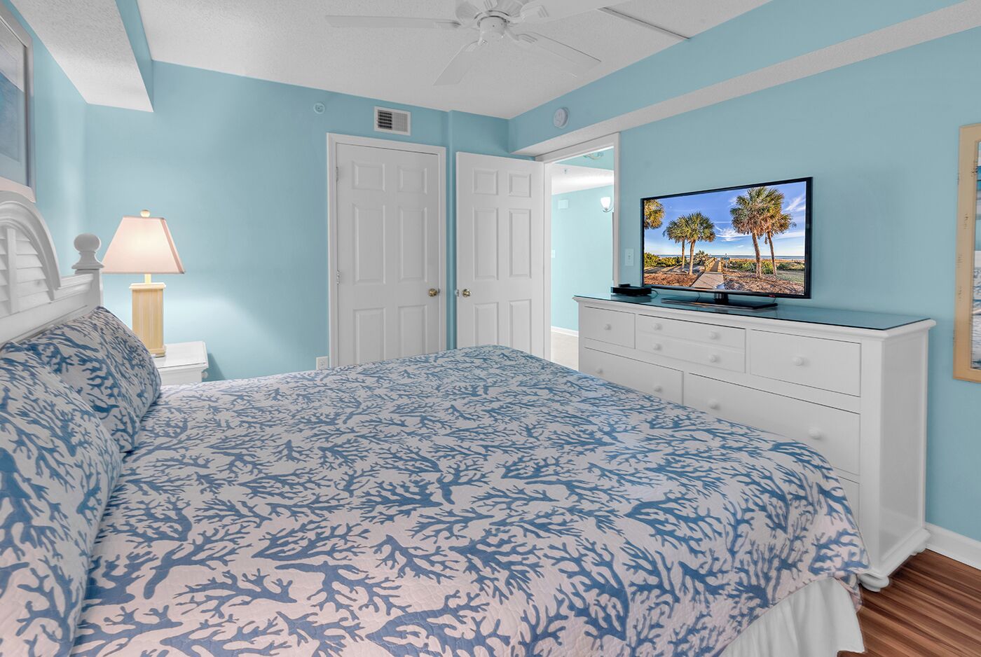 Un dormitorio con cama, cómoda, televisor y ventilador de techo.