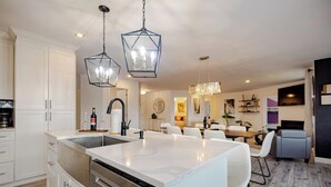 Une cuisine moderne dotée d’un îlot central, de meubles blancs et d’un éclairage suspendu.