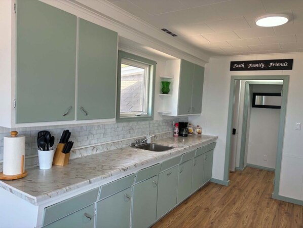 A kitchen with light green cabinets, a marble countertop, and a window.