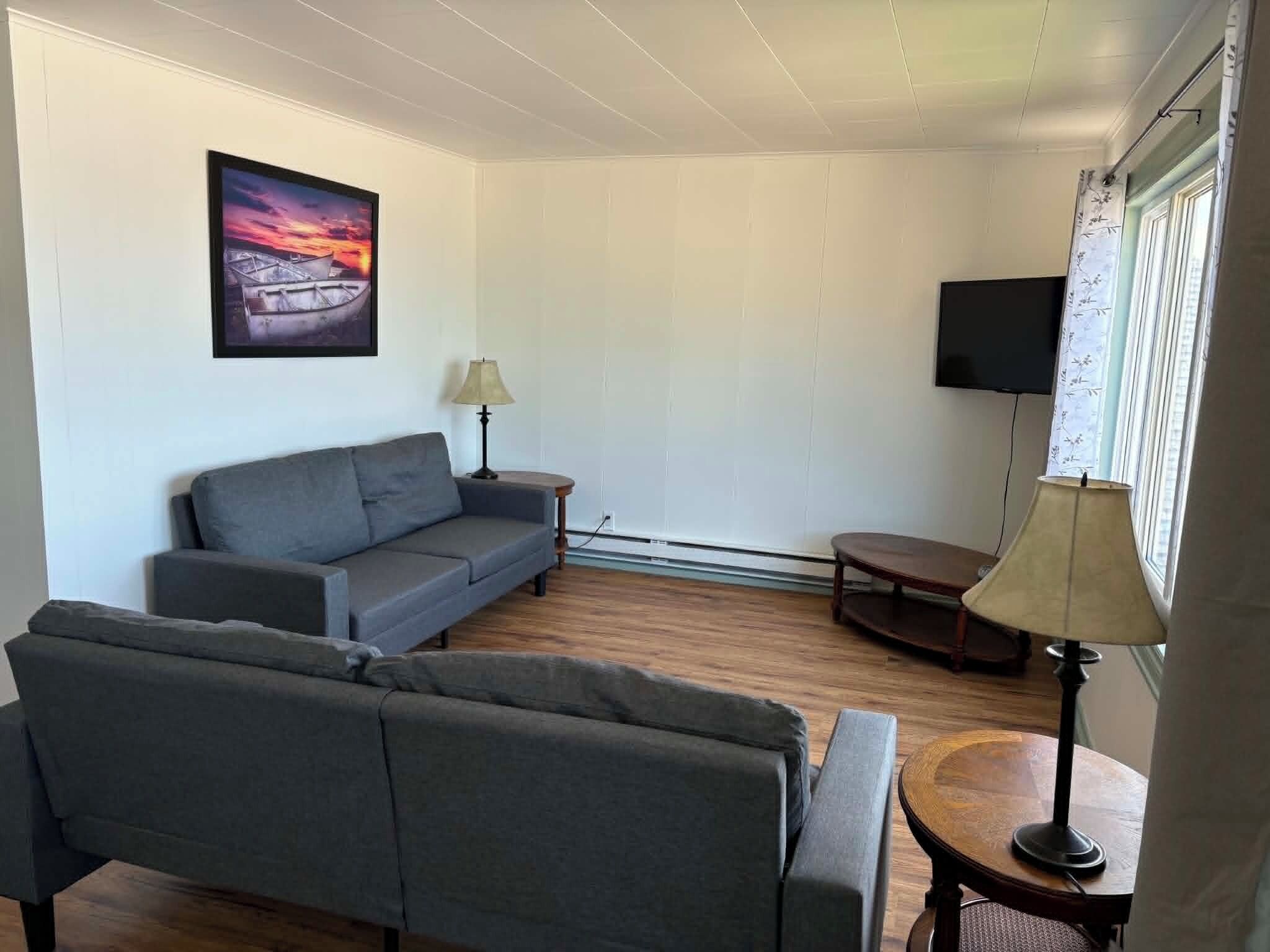 A living room with a sofa, a small table, a lamp, a TV, and a window with curtains.