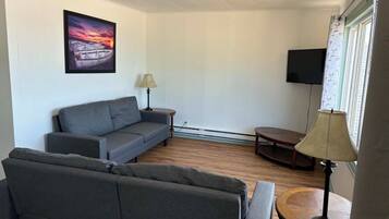 A living room with a sofa, a small table, a lamp, a TV, and a window with curtains.