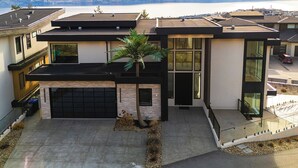 A modern two-story house with a garage, large windows, and a view of mountains and a lake.