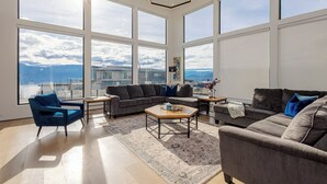 A spacious living room with large windows, a sectional sofa, a coffee table, and a blue armchair.