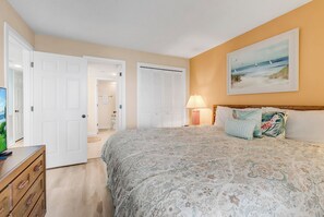 A bedroom with a bed, a dresser, a door leading to a bathroom, and a painting on the wall. - Xanadu III l Ocean front l 1BR Condo l Pool (North Myrtle Beach)