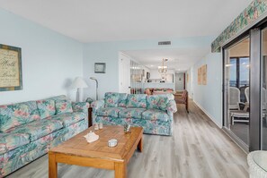 Una sala de estar con sofás florales, una mesa de centro de madera y vista al comedor.