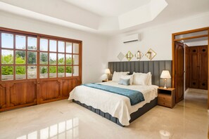 Une chambre avec une grande fenêtre, un lit doté d’une tête de lit grise, des tables de chevet avec des lampes et une armoire.