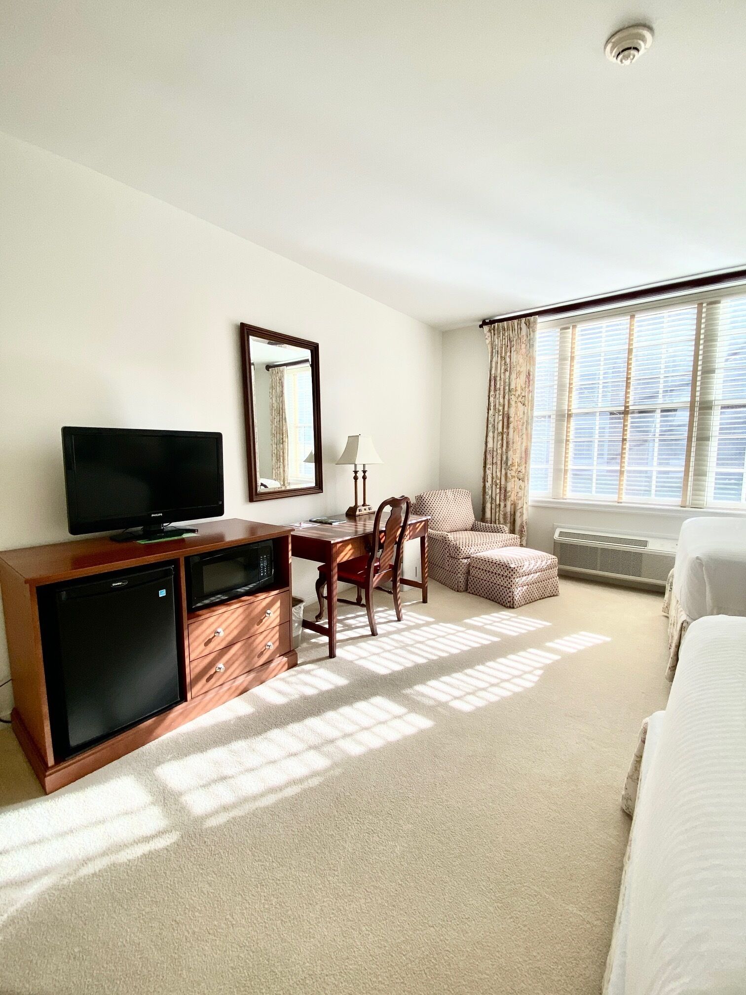 Una camera d'albergo con un letto, una scrivania con una sedia, una televisione, uno specchio e una finestra con tende.