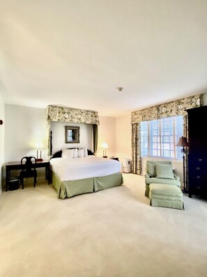 A hotel room with a large bed, a desk, a chair, a dresser, and a window with curtains.