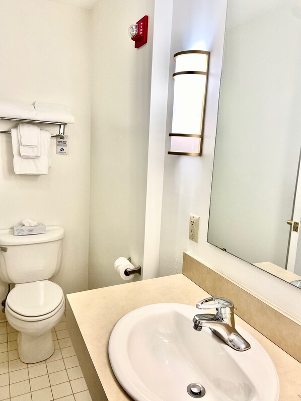 A bathroom with a toilet, sink, towel rack, and a fire alarm. - The Elston Inn and Conference Center (Sweet Briar)