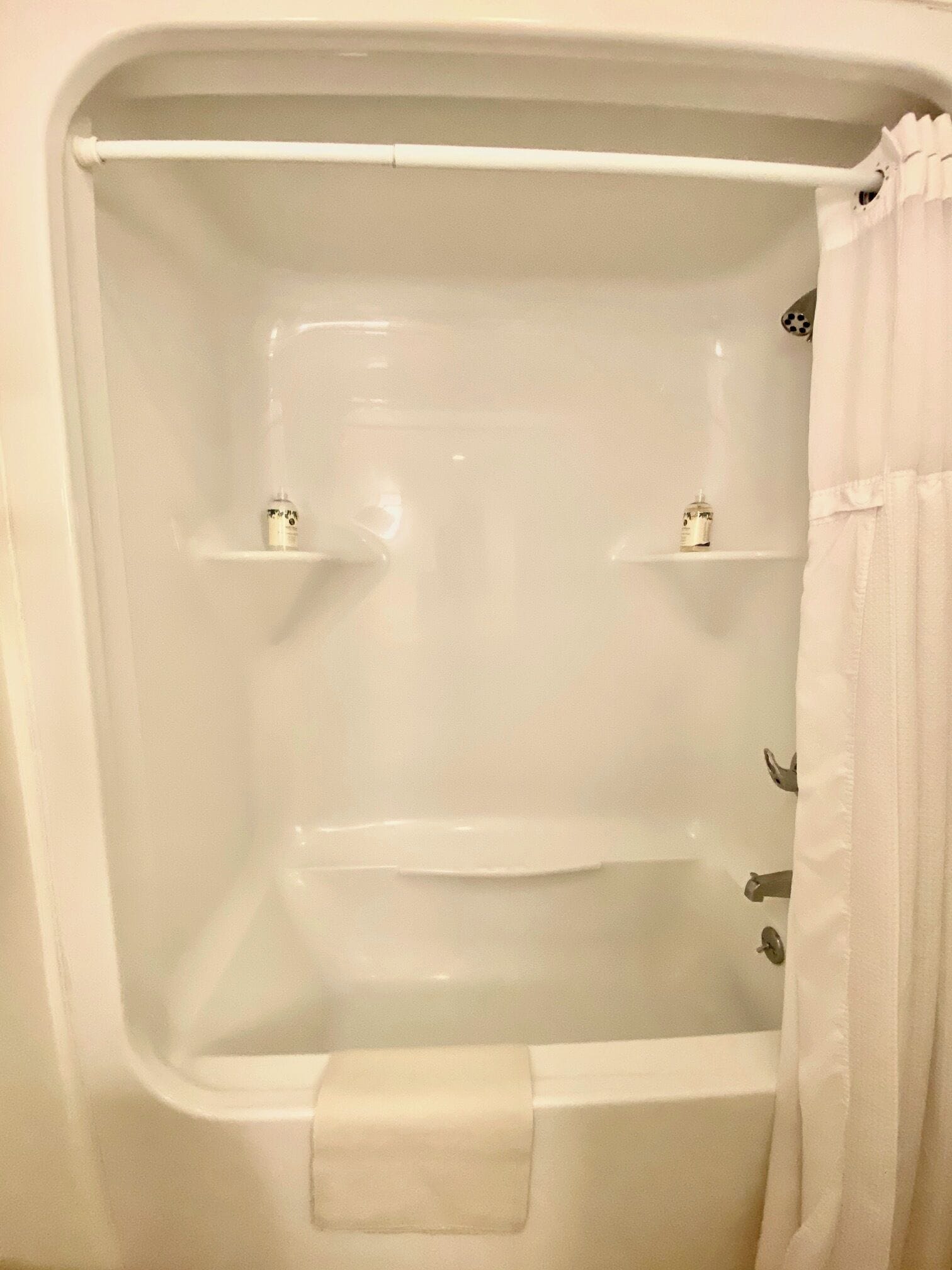 A bathtub with a shower curtain, two shelves, and a towel.