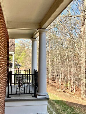 A covered porch with white columns, a brick wall, and a view of a wooded area.
