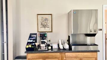 A kitchen area with a coffee machine, a trash bin, and a framed picture on the wall.