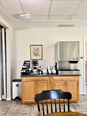 A kitchen area with a coffee machine, a trash bin, and a framed picture on the wall.