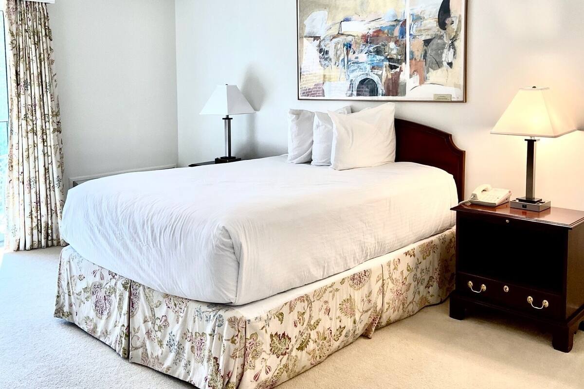 Une chambre à coucher avec un lit, deux tables de chevet, une commode, un tableau et une fenêtre avec des rideaux.