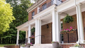 A brick building with a covered entrance labeled 'INN REGISTRATION,' steps leading up to it, and potted plants.