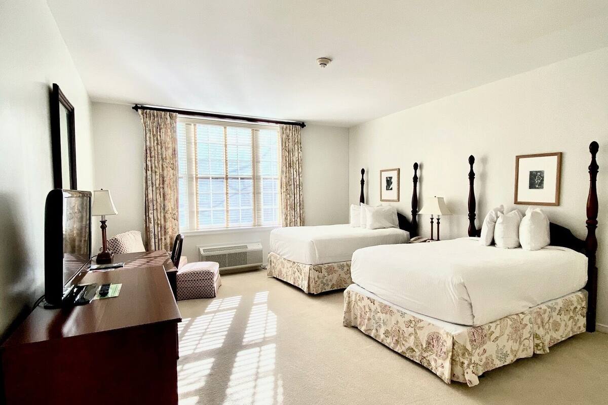 Une chambre avec deux lits, un bureau et une fenêtre avec des rideaux.